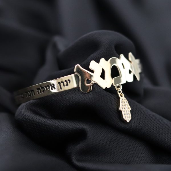 צמיד קשיח עם הכיתוב ״אמא״ ותליון חמסה משובץ אבנים. בצידי הצמיד חריטה של שמות הילדים